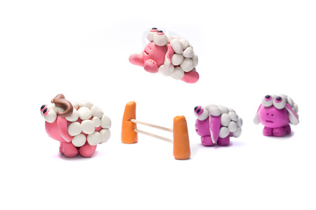 Little plasticine sheep jumping over a fence. White background.の写真素材