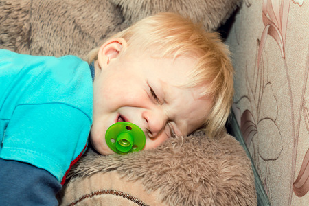 Funny baby lying on the floor with a teddy bear and crying.