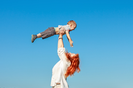 Beautiful red-haired mother playing with her baby. Family fun outdoors.の写真素材