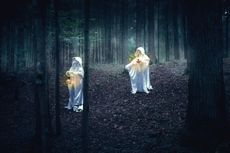 Two figures in white robes with lanterns come in a dark forest.の写真素材