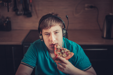 Teenager eating pizza sitting at a laptop. The concept of unhealthy lifestyle.の写真素材