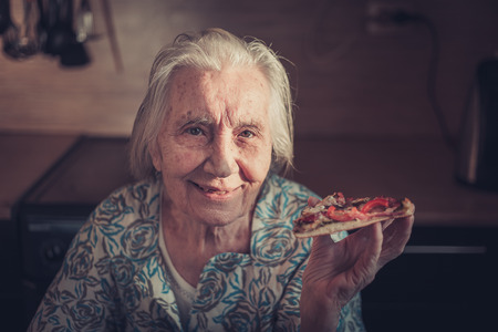 Very elderly woman eating a piece of pizza at home. Unhealthy diets.の写真素材