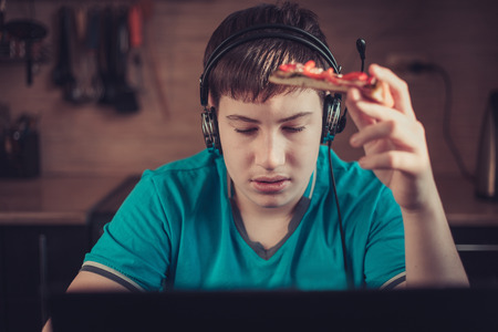 Teenager eating pizza sitting at a laptop. The concept of unhealthy lifestyle.の写真素材