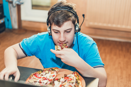 Teenager eating pizza sitting at a laptop. The concept of unhealthy lifestyle.の写真素材