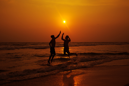 Two men are jumping on the beach. Sunset. The concept of a healthy lifestyle.の写真素材