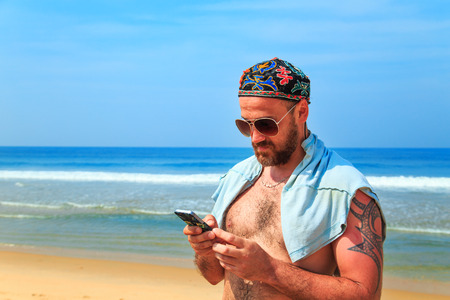 Portrait of a bearded man with a phone against a blue sky.の写真素材