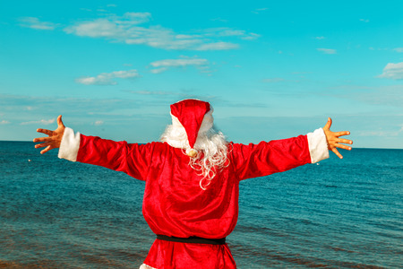 Santa Claus is standing on the beach with arms outstretched. View from the back.の写真素材