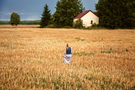 Beautiful blonde girl in a dress in a wheat field. Summer harvest.の写真素材