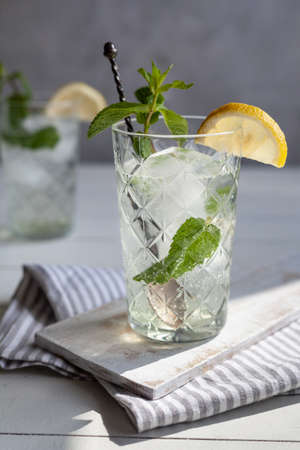 Refreshing drink with lemon and mint in a glass on a white wooden board, one drink in the backの写真素材