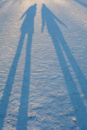 A long winter shadows in the snow of two people standingの写真素材