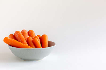 Group of orange carrots in a blue bowl jar on white background, with copy space, vegan snackの写真素材