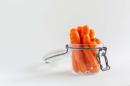 Group of orange carrots in a glass mason jar on white background, with copy space, vegan snack