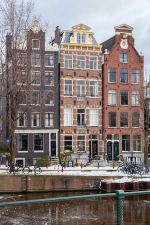 A winter scene of Amsterdam canal houses in the snow with ice on the water, capital in the cold winter season, verticalの写真素材