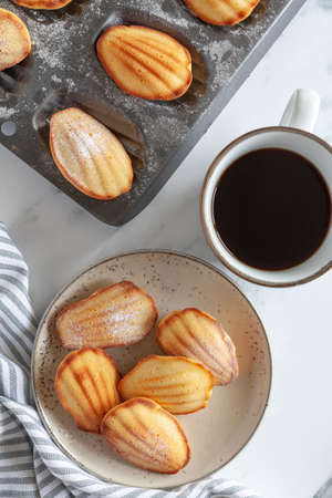 Top down view of freshly baked madeleine sponge cakes with coffee on a white marble surfaceの写真素材