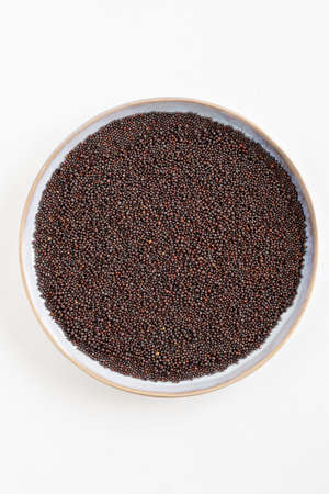 Bird's eye view of a blue plate with black mustard seeds on a white background, Indian cooking ingredient, with copy spaceの写真素材