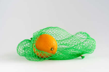 A single orange laying in a green net bag on white background with copy space, horizontal, food shoppingの写真素材