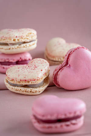 A group of heart-shaped French macaron cookies, vanilla and strawberry flavor, copy space on a pink...