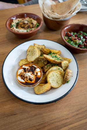 A bowl of za'atar fries with sour cream and chilli oil dip, on a wooden table
