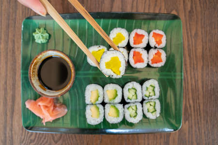 Top down view of a plate of vegetarian sushi, with focus on one piece of sushi held with chopsticks, horizontalの写真素材