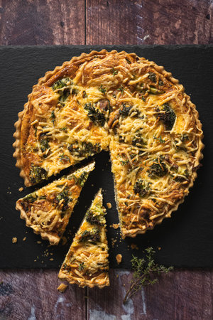 Top down view of a delicious broccoli quiche on black slate background on wooden table, with two slices cut outの写真素材
