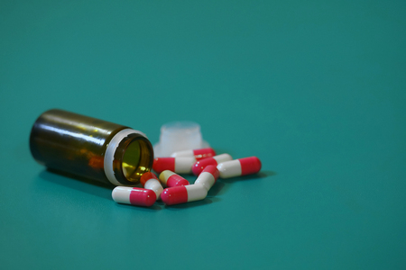 Medication capsules in an opened prescription bottle. Close-up of capsules on green backgroundの写真素材