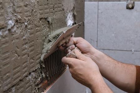 Professional constructor applying glue before laying ceramic tiles on the wallの写真素材