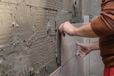 Gluing tiles on the wall. Laying tiles on the wall.  Worker installing big ceramic tiles on the...