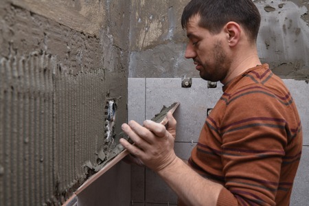 Gluing tiles on the wall. Laying tiles on the wall.  Worker installing big ceramic tiles on the wallsの写真素材