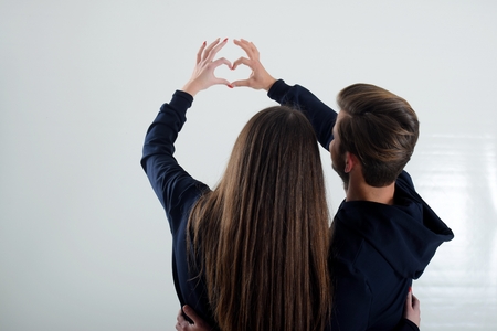 A young couple accepting standing back looking at the white wall shows to the heart. Sensual scene of the young loversの写真素材