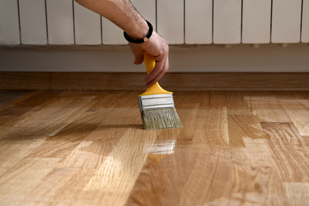 Varnishing lacquering parquet floor by paintbrush - second layer. Home renovation parquet. Varnish paintbrush strokes on a wooden parquet. Application of a highly glossy parquet lacquerの写真素材