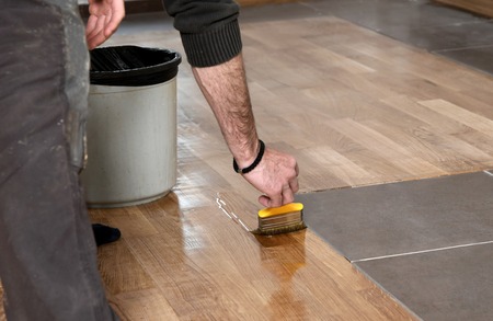 Varnishing lacquering parquet floor by paintbrush - second layer. Home renovation parquet. Varnish...