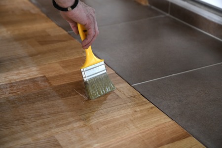 Varnishing lacquering parquet floor by paintbrush - second layer. Home renovation parquet. Varnish paintbrush strokes on a wooden parquet. Application of a highly glossy parquet lacquerの写真素材