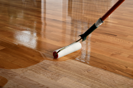 Lacquering wood floors. Worker uses a roller to coating floors. Varnishing lacquering parquet floor by paint roller - second layer. Home renovation parquetの写真素材
