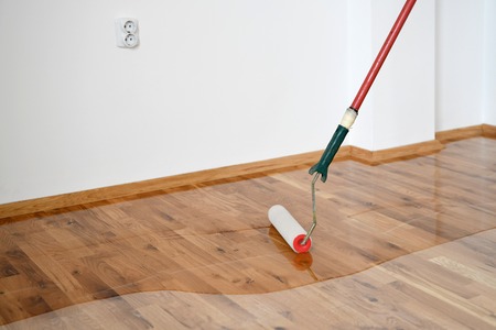 Lacquering wood floors. Worker uses a roller to coating floors. Varnishing lacquering parquet floor by paint roller - second layer. Home renovation parquet