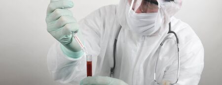 Doctor wearing respiratory mask and holding the Coronavirus Covid-19 blood sample. Scientists test for Covid-19 or Corona virus By using science tubes to research and treat illness in a lab or hospital. Medical treatment conceptsの写真素材