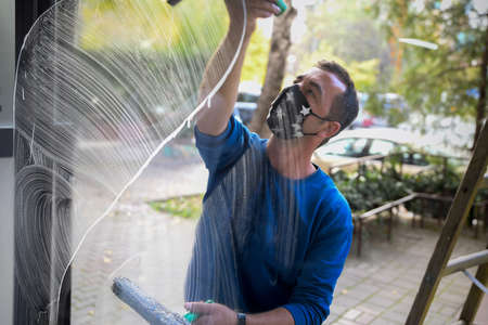 Cleaning the window. A young man with mask on the face cleans and polishes windows with a spongeの写真素材
