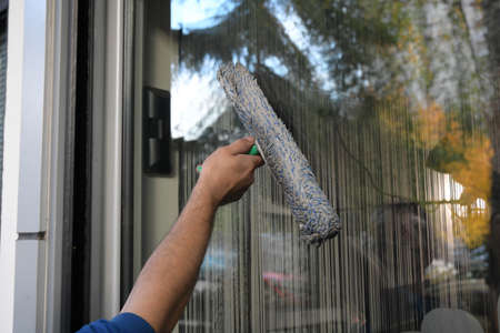 Cleaning the window. A young man with mask on the face cleans and polishes windows with a spongeの写真素材