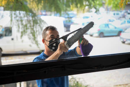 Cleaning the window. A young man with mask on the face cleans and polishes windows with a sponge