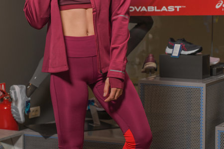 Skopje, Northern Macedonia - March 12, 2021: Asix store in Skopje, Northern Macedonia. Girl photo model wearing a set of dark red tracksuits and sneakers ASICS GEL, standing posing in a sports shopのeditorial素材