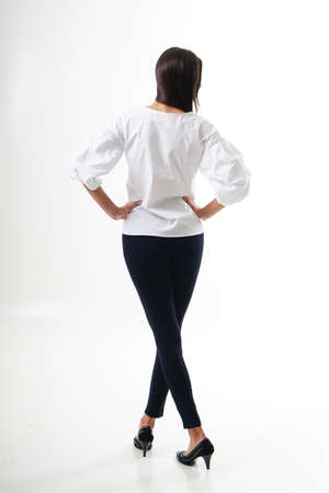 Portrait of woman standing with her back turned, wearing white shirt, black tracksuits with high heels, isolated on white backround. Very attractive woman with unusual and long hair. A girl with beautiful hair turned her back to the audience on a white background.の写真素材