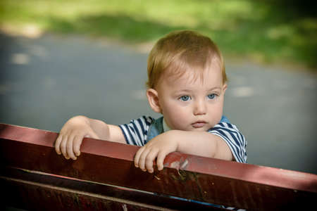 Kid's concept, emotions.Cute little boy staying in park and pensively looking at cameraの写真素材