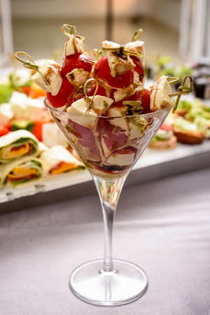 A combination of tomatoes and various types of cheese in a glass cup on the tableの写真素材