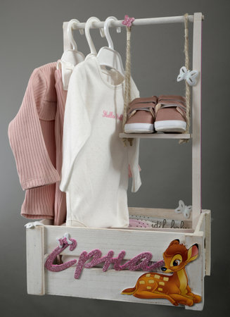 A gift for a newborn baby, placed in a small wooden crate, the shoes placed on a swing. Colorful set of baby romper on gray backgroundの写真素材