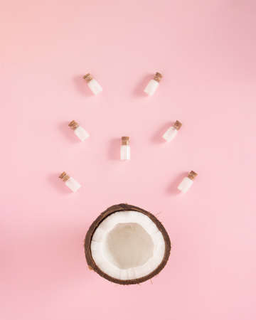 Creative concept of bottles of milkfalls out of fresh coconut. Pastel pink background.の写真素材