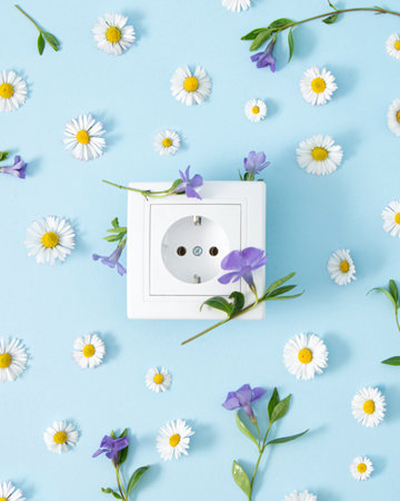 Funny Spring creative concept of power outlet and fresh flowers. Flat lay on pastel blue background.