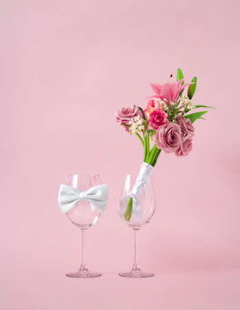 Creative wedding glasses concept the bride with wedding bouquet made of fresh flowers and groom with tie. Pastel pink background.の写真素材