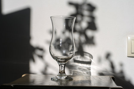 Empty wine glass on a wooden table against a white wall with shadowsの写真素材