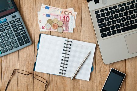 Closeup open notepad with pen, a laptop, a calculator, a smartphone and money on a wooden table. Business conceptの写真素材