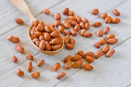 Peanuts in a wooden spoon on a white wooden table