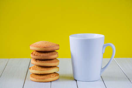 White cup and cookies on a white table on a yellow backgroundの写真素材